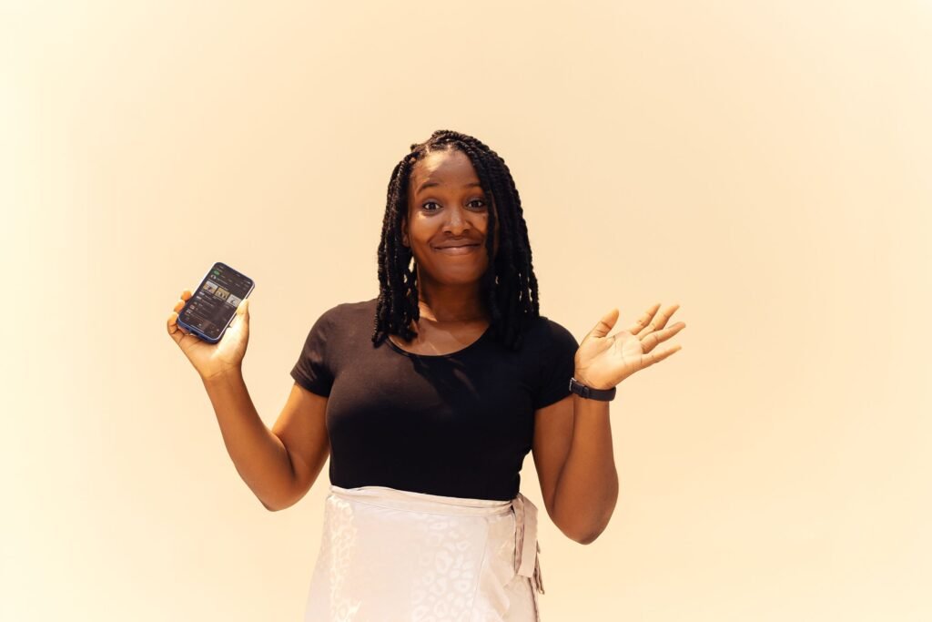 A smiling young woman in Lagos holds up her phone and shrugs, as if choosing between options.
